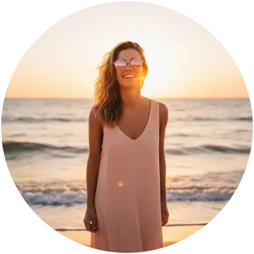 Frau mit verspiegelter Sonnenbrille am Strand bei Sonnenuntergang Glückliche Frau mit verspiegelter Sonnenbrille am Meer bei goldenem Sonnenuntergang – stylischer UV-Schutz für den Sommer
