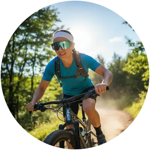 Aktive Frau mit grün verspiegelter Sport-Sonnenbrille beim Mountainbiken im Wald – optimaler UV-Schutz für Outdoor-Sport